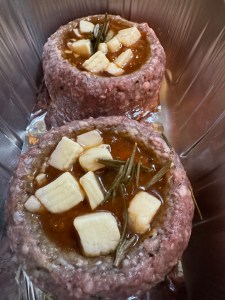 Two raw beef nests filled with red wine ragu sauce, topped with cubes of cheese and sprigs of rosemary, sitting in a foil tray.