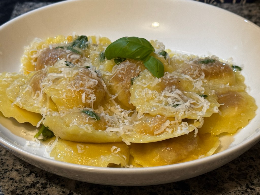 Bowl of White Rabbit Aubergine Parmigiana Girasoli pasta coated in basil butter and topped with grated Parmigiano Reggiano.
