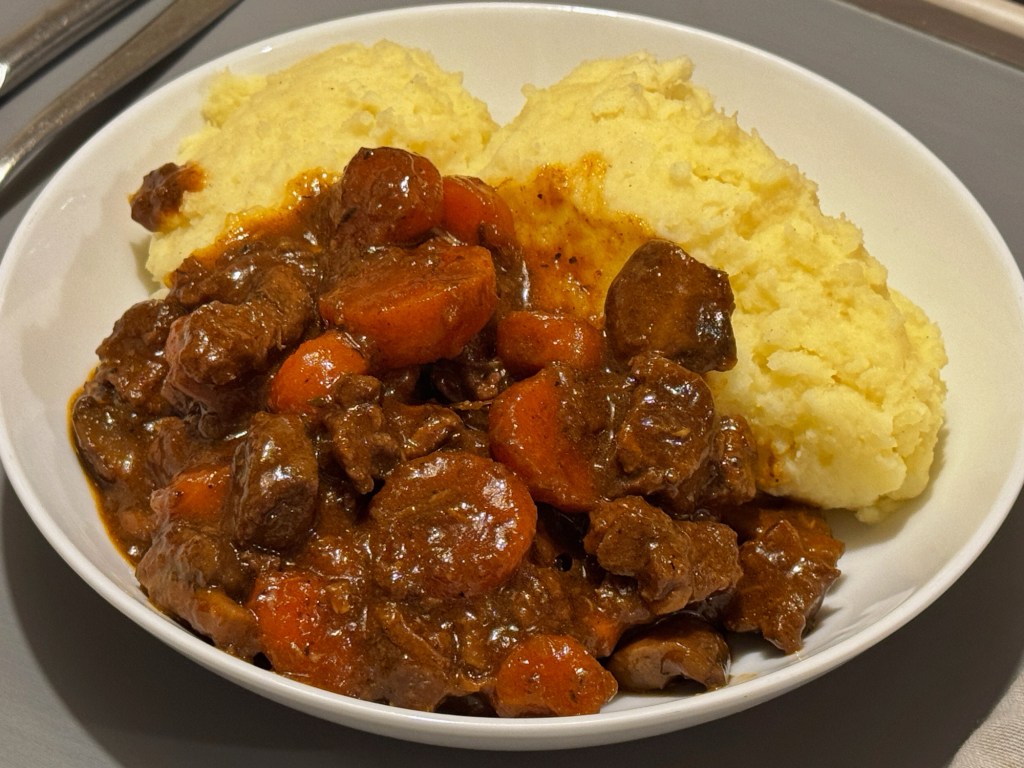 Slow cooker beef and porter casserole with tender beef chunks carrots and mushrooms in a rich gravy served with creamy mashed potatoes.