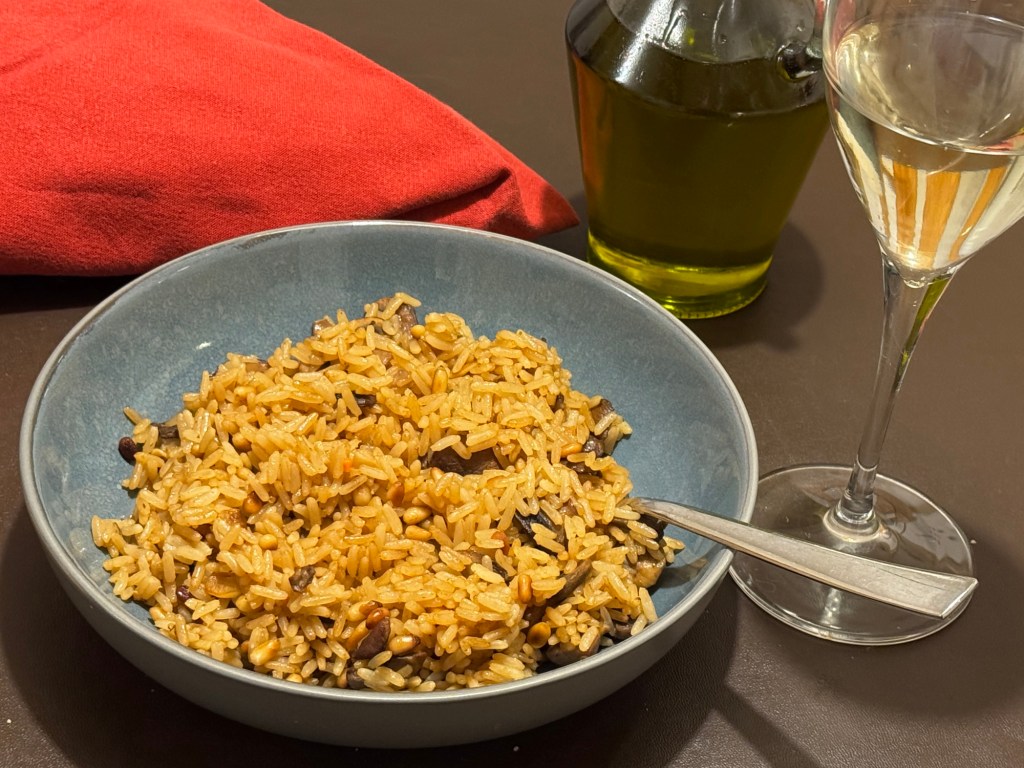 Gluten free garlic mushroom rice with toasted pine nuts served in a blue bowl with a glass of white wine on the table