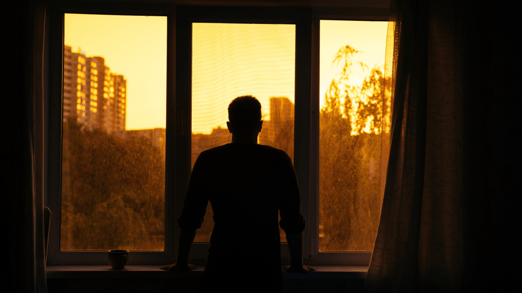 Silhouette of a person standing at a window in warm sunset light reflecting during recovery after being glutened